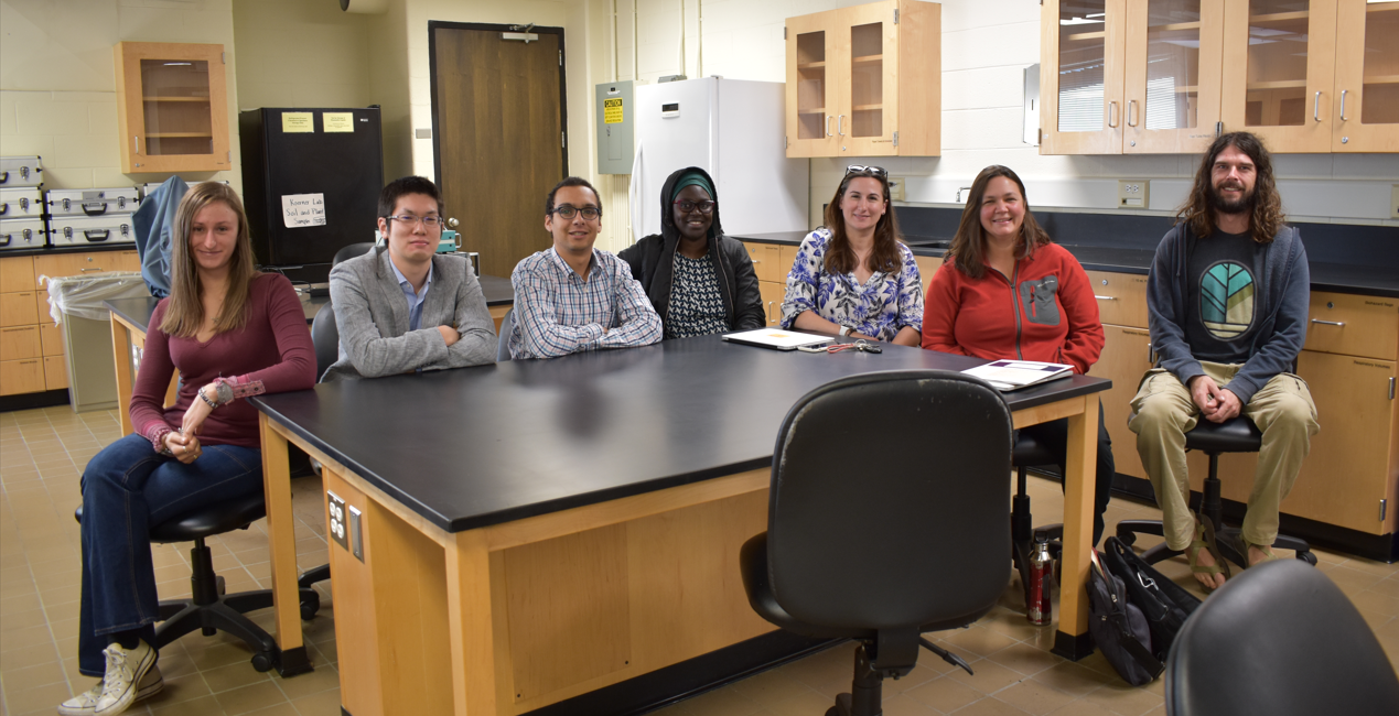Seven research scientists sitting around a lab table smiling at the camera